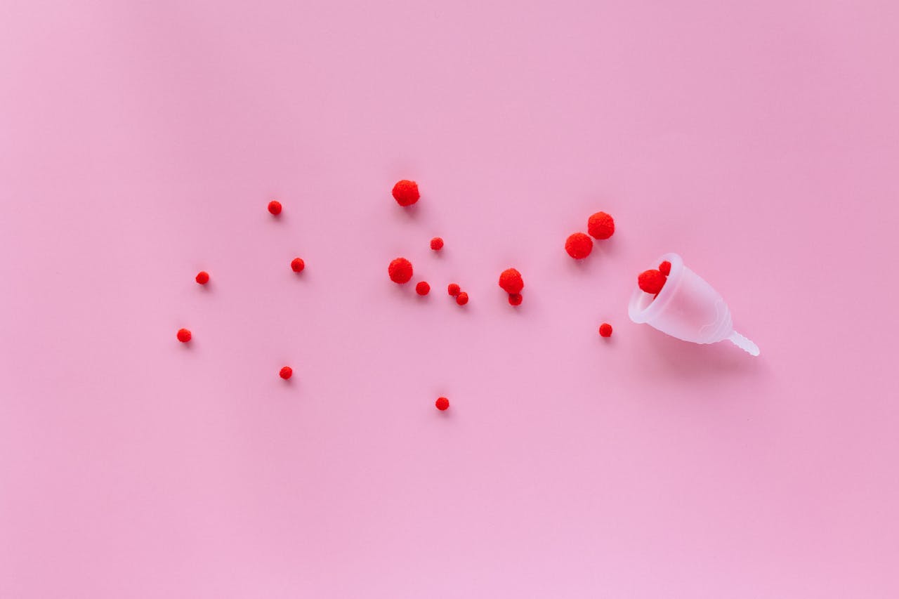 Menstrual cup with red elements on pink background symbolizing menstruation and femininity.